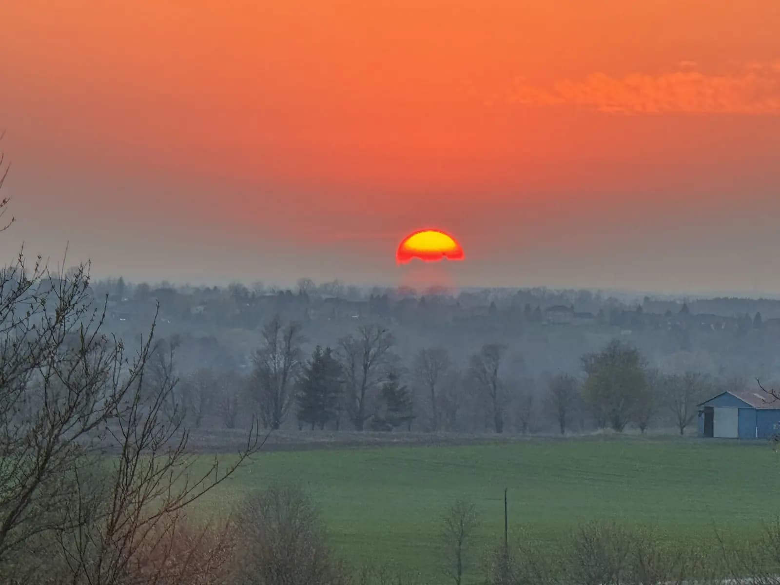 The sun low over the hay fields at the farm, the barn on the treeline