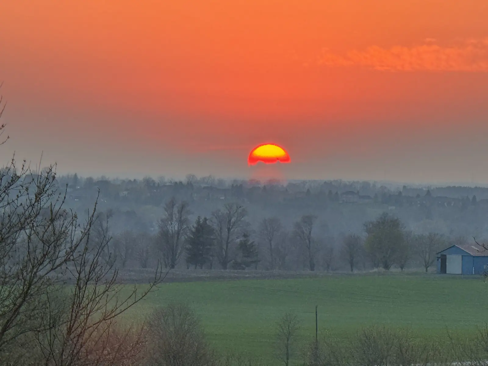 The sun low over the hay fields at the farm, the barn on the treeline